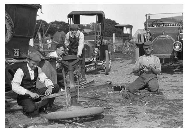 Four gentlemen working on the repair of the touring car at left.